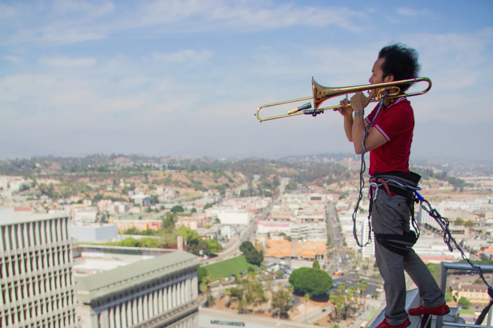 Dana Leong playing trombone while suspended in a harness on the roof of Los Angeles City Hall
